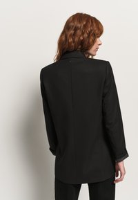 Giacca nera a righe sottili con design su misura, caratterizzata da rever a punte e dettagli sottili sui polsini. Texture liscia e silhouette strutturata.