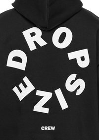 Svart hettegenser med store hvite grafiske bokstaver som danner ordene "DROP" og "CREW" i en sirkulær layout. Myk tekstur.