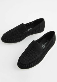 Black suede loafers with woven texture on the upper, featuring a smooth toe and white rubber sole. Slip-on design with perforated accents.