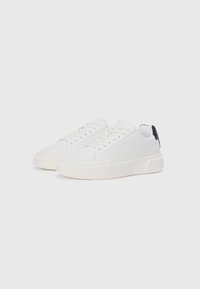 Adidași albi cu brâu din piele netedă, vârf rotund și branding subtil. Prezintă șireturi plate și un accent texturat negru pe toc.