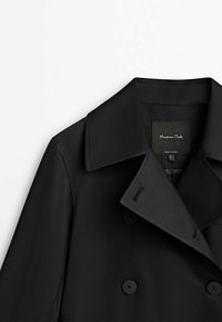 Musta kaksirivinen takki, jossa on suuret kaulukset, sileä kangas ja napituksia. Tunnuslukee "Massimo Dutti."