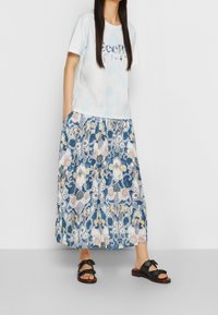 Ljusblå tie-dye t-shirt med tryckt mönster, kombinerad med en lång maxikjol med blommönster i blått, kräm och guld. Svarta sandaler.