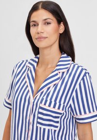 Short-sleeve pajama shirt in navy and white stripes, featuring a notched collar, single pocket, and light pink piping along edges.