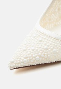 Chaussure blanche pointue recouverte de petites et grandes perles nacrées et d'une fine bordure en cuir le long du bord d'ouverture.