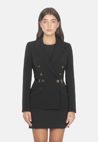 Blazer neri su misura doppiopetto con bottoni dorati, tasche laterali e silhouette aderente. Tessuto morbido e design strutturato.