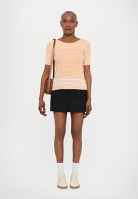 Perzikkleurig gestreept gebreid topje met een bootnek, gecombineerd met een zwarte minirok met voorzakken en knopen. Witte sokken en beige sneakers maken de look compleet.