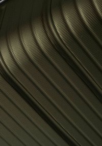 Valigia rigida verde scuro con superficie testurizzata caratterizzata da scanalature verticali e un motivo geometrico, che migliora la presa e la durabilità.