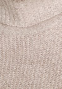 Lichtbeige gebreide coltrui met een zachte, fuzzy textuur. Kenmerkt zich door een geribbeld ontwerp bij de hals en het lichaam met losse steken.