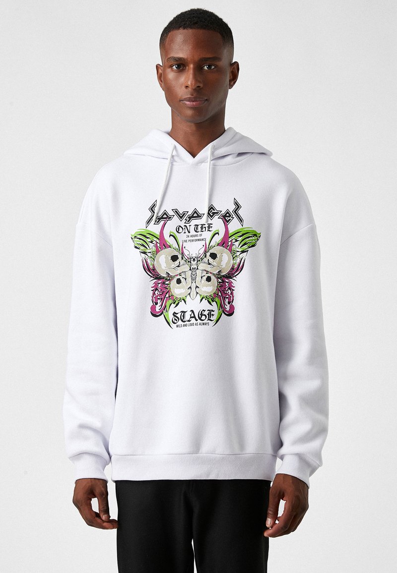 Sudadera blanca con un diseño gráfico que incluye calaveras, una mariposa y el texto "SAVAGE ON THE STAGE". Hecha de una tela suave con puños acanalados.