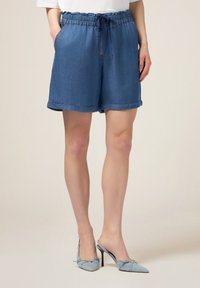 Pantaloni corti in denim con vita elasticizzata e cordoncino, di un blu medio. Presentano tasche laterali e orli arrotolati per una vestibilità comoda.