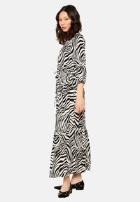 Lungo abito a strisce zebra in nero e beige, con vita stretta, maniche a tre quarti e gonna a strati. Abbinato a scarpe nere.