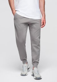 Grå joggingbyxor i mjukt material, med avsmalnande ben och ribbade muddar. Bärs med ljusa sportskor.