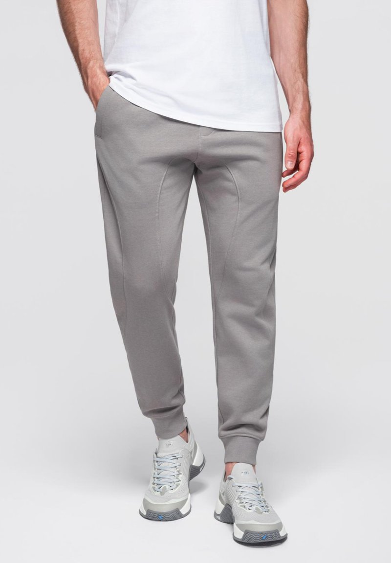 Grå joggingbyxor i mjukt material, med avsmalnande ben och ribbade muddar. Bärs med ljusa sportskor.