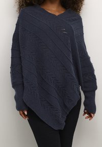 Marinblå stickad poncho med V-ringning, med diagonala texturmönster och öppna stickade sektioner, utrustad med långa ärmar och tumhål.