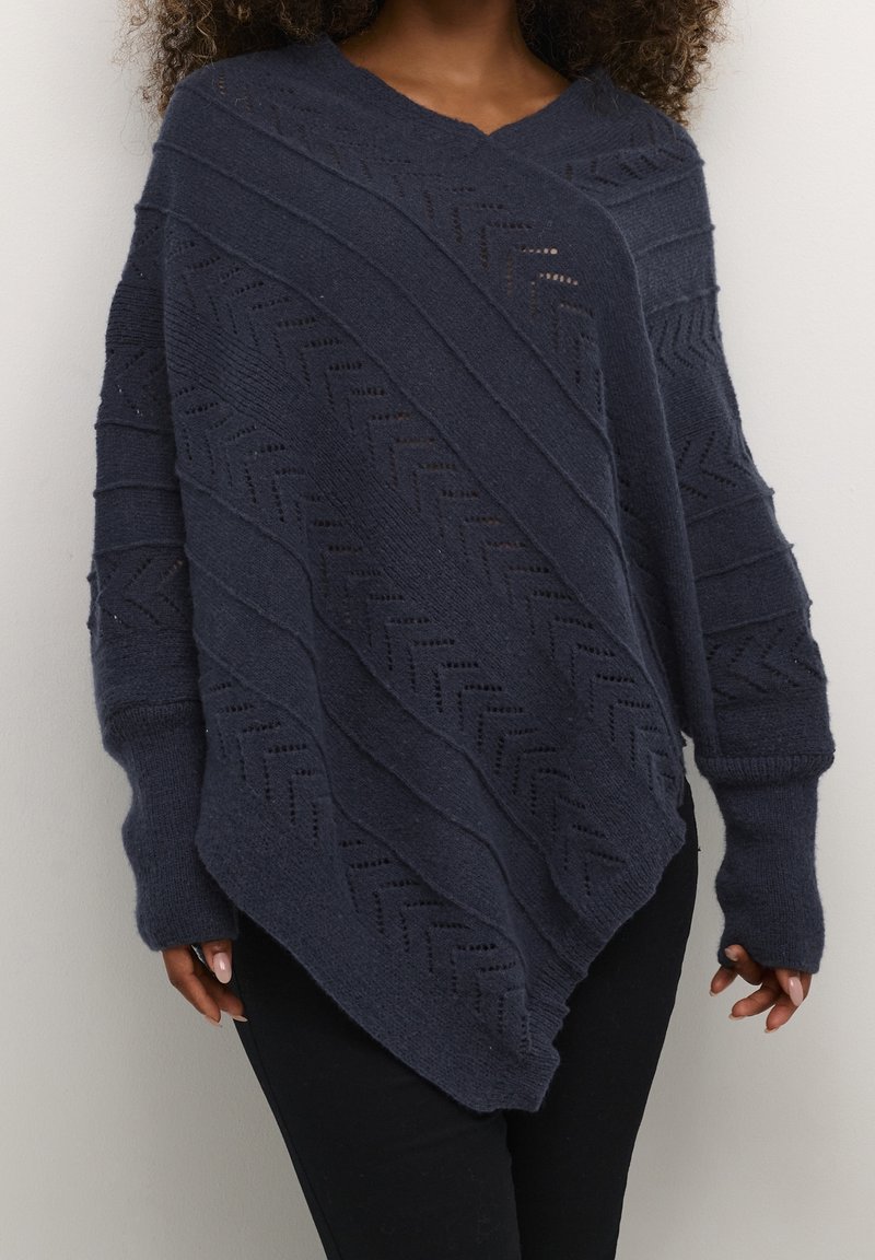Marinblå stickad poncho med V-ringning, med diagonala texturmönster och öppna stickade sektioner, utrustad med långa ärmar och tumhål.
