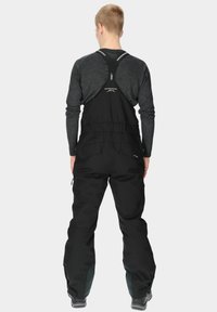 Black bib overalls with adjustable straps, zippered pockets, and reinforced panels at the ankles. Made from durable, water-resistant material.