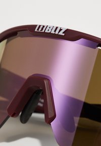 Okulary przeciwsłoneczne z bordową oprawą, lustrzanymi fioletowymi soczewkami, ergonomicznym mostkiem nosowym oraz logo "BLIZ" na górze. Smukły, nowoczesny design.