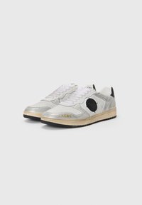 Zapatillas deportivas con una combinación de colores plateado y gris, material sintético, cordones blancos, un logo circular negro y una suela texturizada negra.
