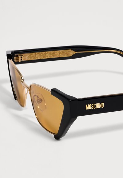 Μαύρα και χρυσά γυαλιά ηλίου Moschino με κεχριμπαρένιους φακούς και λεπτομερή χρυσό σχέδιο στο εσωτερικό του βραχίονα.