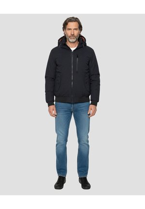 Zwarte jas met ritssluiting en capuchon, met rode accenten, voorzien van twee zijzakken en één met rits afsluitbare borstzak. Draagt blauwe spijkerbroek en zwarte schoenen.