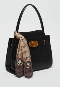 Sac à main structuré noir avec une fermeture dorée et un foulard beige et marron à motifs noué à une anse, sur un fond clair.