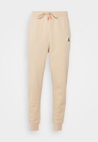 Beiga joggers i mjukt material, med dragsko i midjan, smalnande muddar och en framträdande logotyp på vänster lår.