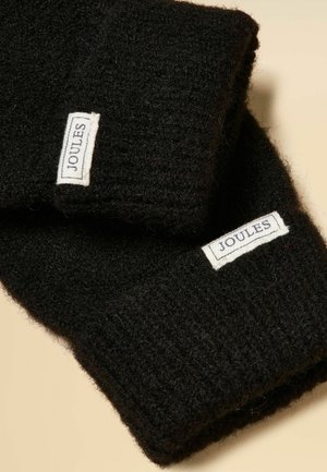 Sorte strikkede handsker med hvide, rektangulære Joules-mærker syet nær håndleddet på en beige baggrund.