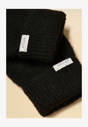 Sorte strikkede handsker med hvide, rektangulære Joules-mærker syet nær håndleddet på en beige baggrund.