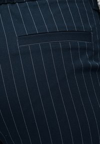 Κοντινό πλάνο υφάσματος σε ναυτικό μπλε με κάθετες ρίγες, που διαθέτει οριζόντια τσέπη με λευκές ραφές.