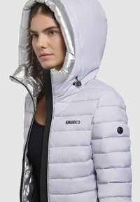 Lichte gewatteerde jas in pale lavendel met een glanzende zilveren binnenvoering, voorzien van een ritssluiting en subtiele logo-accenten.