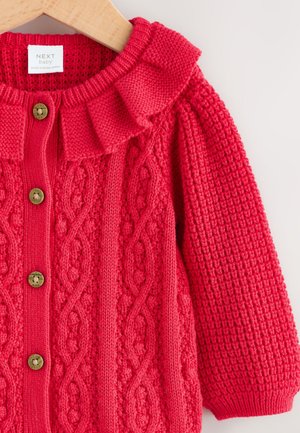 Punane kootud kardigan, millel on volangidega ääristatud krae, nööpkinnitus ja tekstuuriga mustrid, varrukaotstes soonikkoes äärised ja palmiku muster.