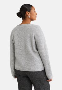 Grau gestrickter Pullover mit lockerer Passform, langen Ärmeln und weitem Ausschnitt, kombiniert mit dunkel strukturierten Hosen, von hinten gezeigt.