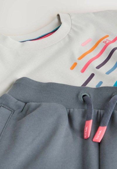 Lysegrå skjorte med farverige bølgede striber ved siden af mørkegrå sweatpants med ribbet taljebånd og snore med lyserøde ender.