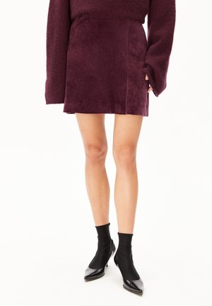 Bordeauxfarbene Minirock aus weichem, wildlederähnlichem Stoff, mit einem schlichten Design, klaren Linien und einer taillierten Silhouette. Getragen mit schwarzen Ankle Boots.