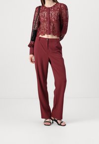 Top corto de encaje burdeos con diseño floral y cierre de botones, combinado con pantalones burdeos de rayas finas y sandalias planas negras.