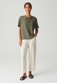 Top corto a maniche corte verde oliva con scollatura a chiave, abbinato a pantaloni a gamba larga color beige chiaro e sandali neri aperti. Tessuto dalla consistenza liscia.