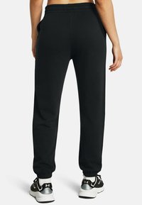 Zwarte sportieve joggers met een elastische tailleband en boorden, voorzien van zijzakken en een gladde textuur, gedragen met zwarte sneakers.