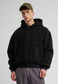 Sweat à capuche en polaire noire avec une poche kangourou, des poignets côtelés et un ourlet côtelé. Dispose d'une capuche avec cordon de serrage et d'un tissu texturé pour plus de chaleur. Coupe décontractée.