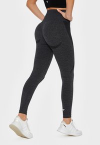 High-rise black leggings with a textured finish, seamless design, and a snug fit, paired with white athletic shoes.