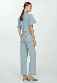 Jumpsuit dżinsowy w jasnoniebieskim kolorze, z krótkimi rękawami, elastycznym paskiem w talii, prostymi nogawkami oraz bocznymi kieszeniami z detalami szwów.