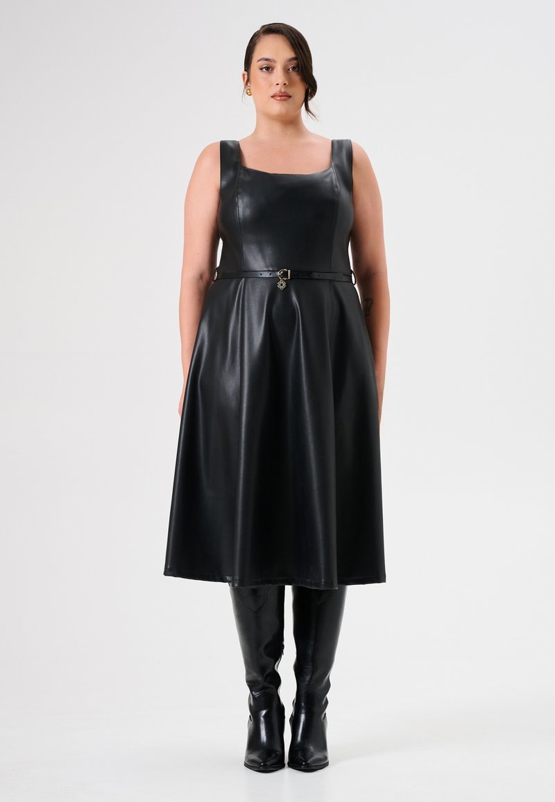 Zwarte faux leren jurk met vierkante halslijn, brede bandjes en ceintuur in de taille. Bevat een vloeiende rok en zwarte kniehoog boots.