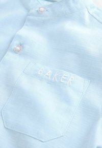 Svetlo modra srajca z teksturirano vzorcem, z gumbasto ovratnikom in prsno žepno, ki ima izvezeno ime "BAKER".