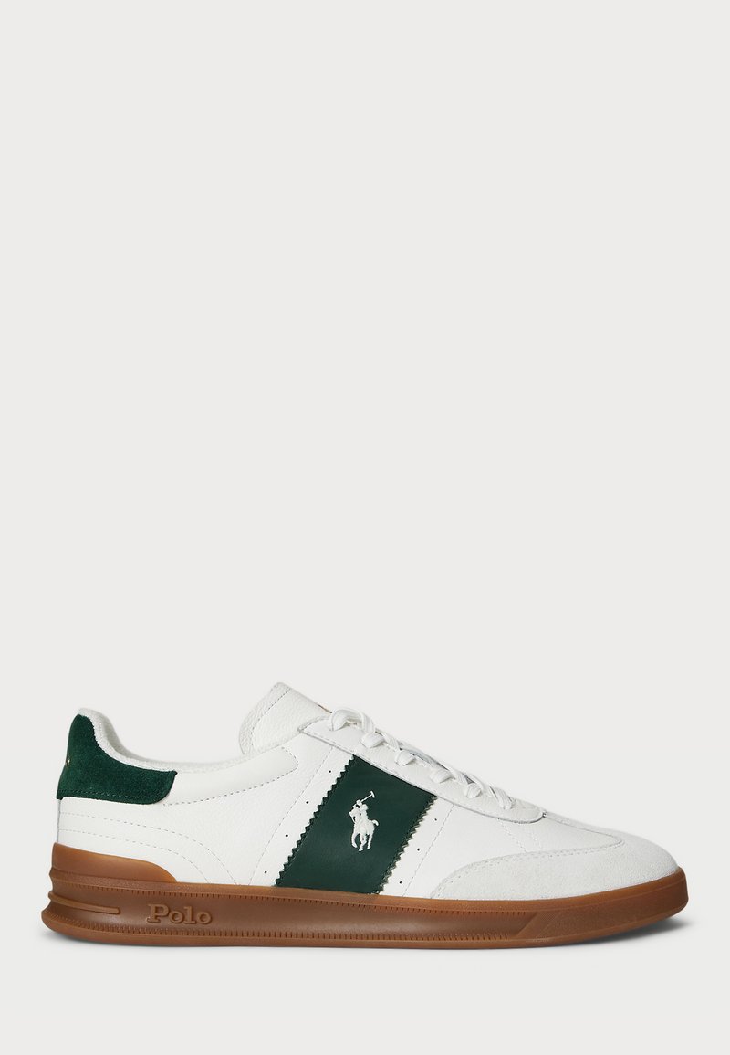 Hvite sneakers med grønne detaljer, med en panel i semsket skinn, snøring foran og brun gummisåle. Brodert logo på siden.