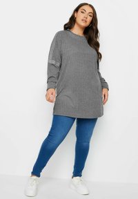 Grå ribbad tröja med långa ärmar, med nitar på axlarna, tillsammans med blå smala jeans och vita sneakers.