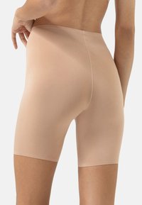 Shorts beiges, fabriqués en matériau lisse et extensible. Présentent une coupe mi-cuisse et un design sans coutures avec une légère brillance. Détails de couture minimaux.