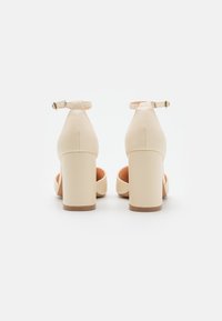 Beige korkokengät, joissa on paksu korko, nilkkahihna ja sileä synteettinen materiaali. Sisäpuolella on pehmeä, kevyesti pehmustettu oranssi vuori.