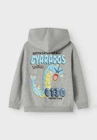 Pelēks sporta krekls ar Gyarados grafiku no Pokémon. Dizainā ietilpst zila, dzeltena un melna krāsa, kā arī teksti "0130" un "VANDENS TIPS".