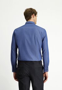 Niebieska koszula wzorzysta z długimi rękawami i mankietami zapinanymi na guziki, w połączeniu z ciemnymi, teksturowanymi spodniami, widoczna z tyłu.