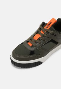 Olive green sneaker with mesh and leather materials, black accents, thick black rubber sole, and bright orange laces and tag.