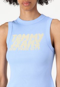 Top senza maniche blu a coste con una stampa grafica audace di colore giallo chiaro che recita "TOMMY JEANS NEW YORK CITY" sul petto.